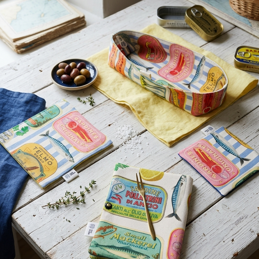 paneras alargadas confeccionadas a mano de algodon de rayas beige y azules y estampado de latas sardinas aceitunas y Gildas esta combinada con posavasos servilletas y funda para cubiertos