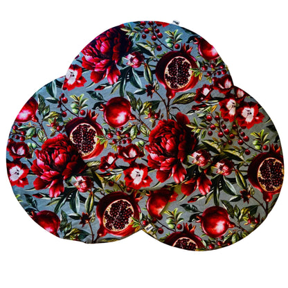 Mantel individual redondo reversible de algodón con estampado floral de granadas en tonos rojos y fondo verde agua. Diseño elegante y original para vestir la mesa con personalidad.
