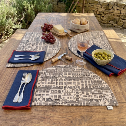 mesa puesta aesthetic con manteles individuales semicirculares con estampado de casitas y relleno. combinados con servilletas de mezcla de lino en azul marino y ribete rojo personalizares con frase.