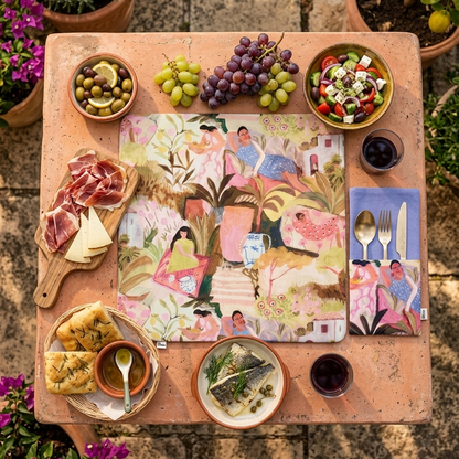 mesa puesta con mantel estampado cuadrado de mujeres en un jardín y reves lavanda. servilleta a juego con bolsillo en los mismos colores y estampado 