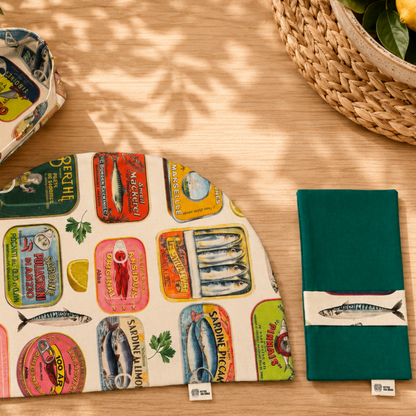 servilleta con guardascubiertos en tejido de algún verde reversible y tira en ella estampada de algodon beige con dibujos de sardinas y latas combinada con mantel media luna y panera del mismo estampado reversible