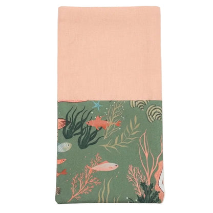 servilleta con bolsillo con estampado de sirenas peces y corales en tonos verdes y naranjas, combinada con tejido de algodón en tono melocotón 
