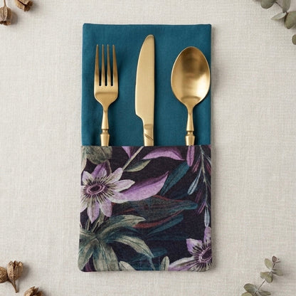 servilleta de algodón en azul petroleo con bolsillo estampado de flores passifloras en tonos verdes y malvas con cubiertos dorados dentro del bolsillo